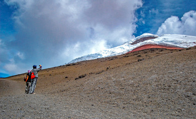 Two people observing and photographing the Cotopaxi volcano from it's slopes, on a sunny and cloudy afternoon. Cotopaxi National Park, Ecuador.