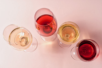 A set of rose and white wine in a glasses on pink background, flat lay.