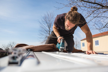 Man using a jigsaw to saw into the roof of a van