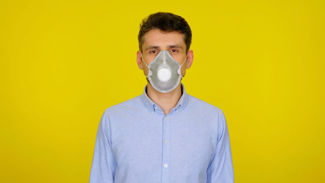Man in protective respiratory mask looks at the camera. The guy in the blue shirt on a yellow background. Concept against the virus: Coronavirus, flu - Powered by Adobe