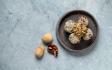 Fototapeta premium Oatmeal, energy balls covered with sesame and walnut crumbs, lie on a ceramic plate, next to pecans . Top view, copy space, healthy food, trend..
