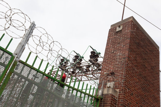Angled view of power substation enclosure with old brick and wrought iron security enhanced with modern razor wire, horizontal aspect