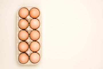 A tray of brown fresh hen's eggs on beige background. Eco-friendly egg production. Baking ingredients. Organic chicken eggs - fresh from producer. Top view.  Free space for text. 