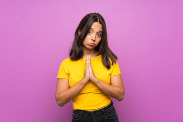 Young brunette girl over isolated background keeps palm together. Person asks for something