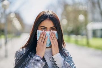 Girl putting on a protective mask to avoid contagion while walking down the street. Coronavirus...