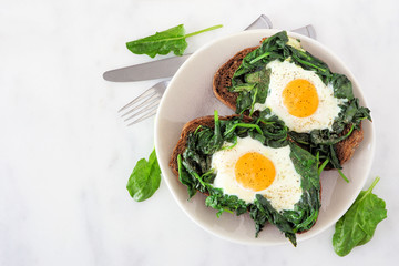Healthy toasts with spinach and egg  on a plate. Top view over a white marble background.
