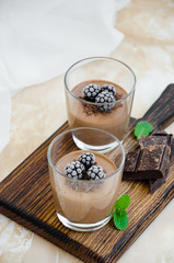 Italian dessert - chocolate panna cotta, mousse, cream or pudding with blackberry in a glass on a board on a light concrete background. Vertical orientation. Copy space