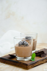 Italian dessert - chocolate panna cotta, mousse, cream or pudding with blackberry in a glass on a board on a light concrete background. Vertical orientation. Copy space