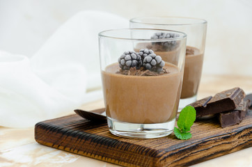 Italian dessert - chocolate panna cotta, mousse, cream or pudding with blackberry in a glass on a board on a light concrete background. Horizontal orientation. Copy space