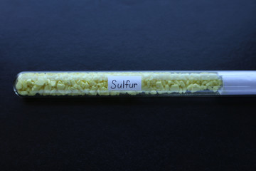 Yellow crystalline sulfur, a simple solid, in a test tube on a black background.