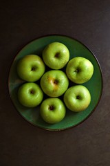Green apples on a green plate.  Bright green apples on a green plate with a black rim against a dark grey background.