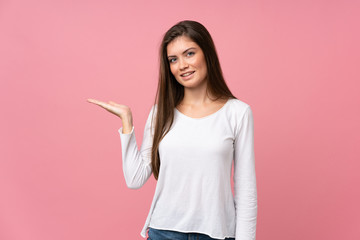 Young woman over isolated pink background holding copyspace imaginary on the palm to insert an ad