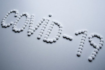 Text phrase Covid-19 sign concept made from white pills on a white background
