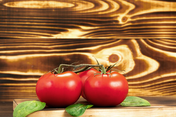 Red tomatos on a cutting board with basil leaves on wooden background. Fresh vegetables for cooking, copy space