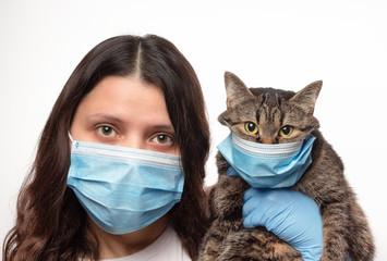 Girl with cat in protective medical masks on white background. Caring for animals during the...