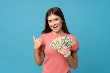 Young woman over isolated blue background taking a lot of money