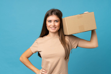 Young woman over isolated blue background holding a box to move it to another site