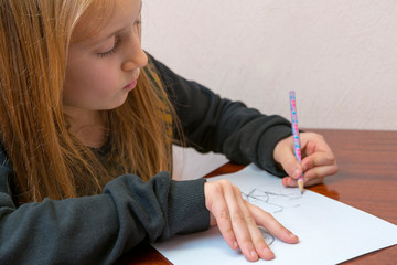 Schoolgirl draws at a desk. Little girl student studying sitting at her desk. School, education, knowledge and children. toned