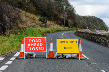 Road closed signs on a coastal road due to fallen rocks.