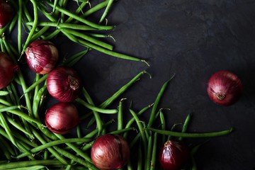 Green beans and red onions scattered across a dark grey background.  Landscape flat lay or top view for perfect background with space for text. © Angela