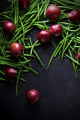 Green beans and red onions scattered across a dark grey background.  Portrait flat lay or top view for perfect background with space for text.