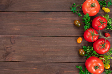 Red tomatoes and cherry tomatoes of different colors with parsley leaves on rustic wooden surface with copy space. Fresh vegetables, bio food