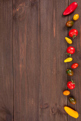 Vertical top view of fresh vegetables. Red, green, yellow cherry tomatoes and mini peppers on rustic wooden background with copy space