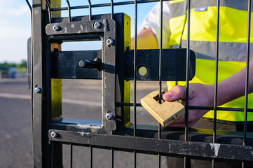 A security guard attaches a lock to a gate after unlocking the bolt and opening the gate