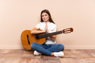 Young woman with guitar sitting on the floor pleading