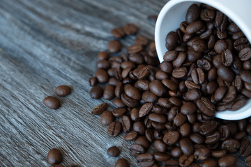 Coffee beans fall out of a cup on a wooden table.