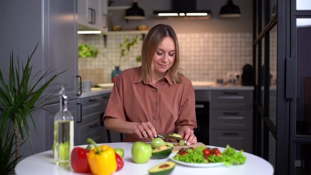 Young smiling vegetarian woman preparing healthy vegan food alone at home. Attractive fit girl prepare healthy dinner, make surprise for husband. Healthy food lifestyle concept. Shooting in slowmotion