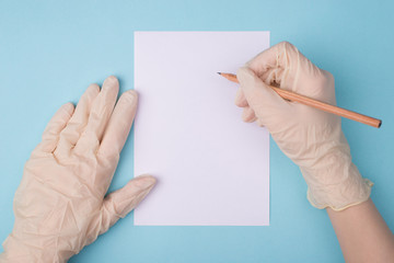 Cropped close up first person view photo of hands in protective white rubber gloves writing on empty paper with a pen isolated on blue background