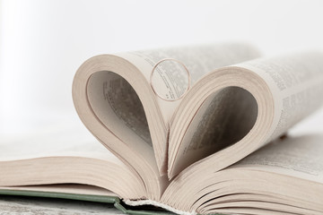 Pages of book are twisted as a heart sign with gold ring