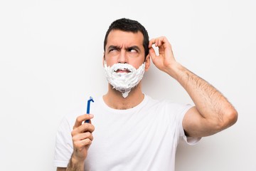 Man shaving his beard over isolated white background having doubts while scratching head