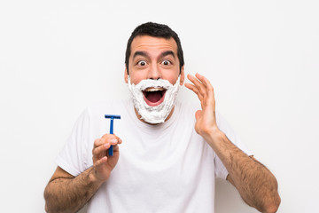 Man shaving his beard over isolated white background with surprise and shocked facial expression