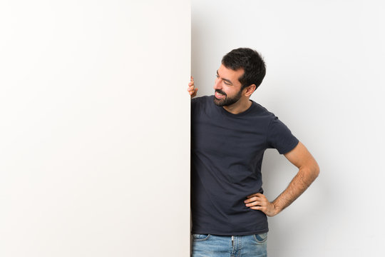 Young handsome man with beard holding a big empty placard looking to the side