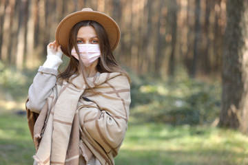 young stylish woman in medical protective mask from COVID-19, coronavirus outdoors. Girl in the forest. Air pollution, environmental concept. selective focus