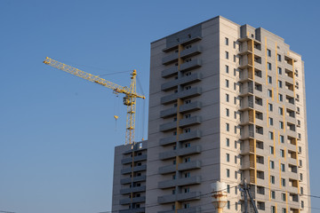 Fototapeta na wymiar Modern building under construction with crane. From below of constructing building with high crane under clear sky