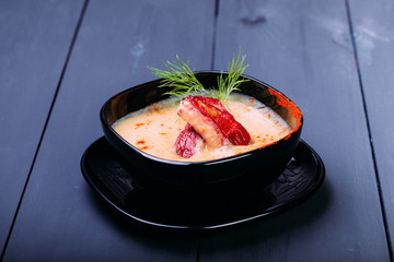 Cream soup with pieces of fish or salmon fillet in a black dishes on a wooden table. chinese food, soup. Front view