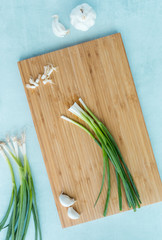 A top down view of green onion and garlic cloves on a wooden cutting board. 
