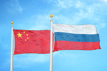 China and Russia two flags on flagpoles and blue cloudy sky