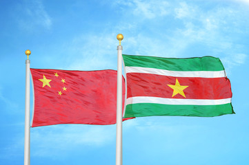 China and Suriname two flags on flagpoles and blue cloudy sky