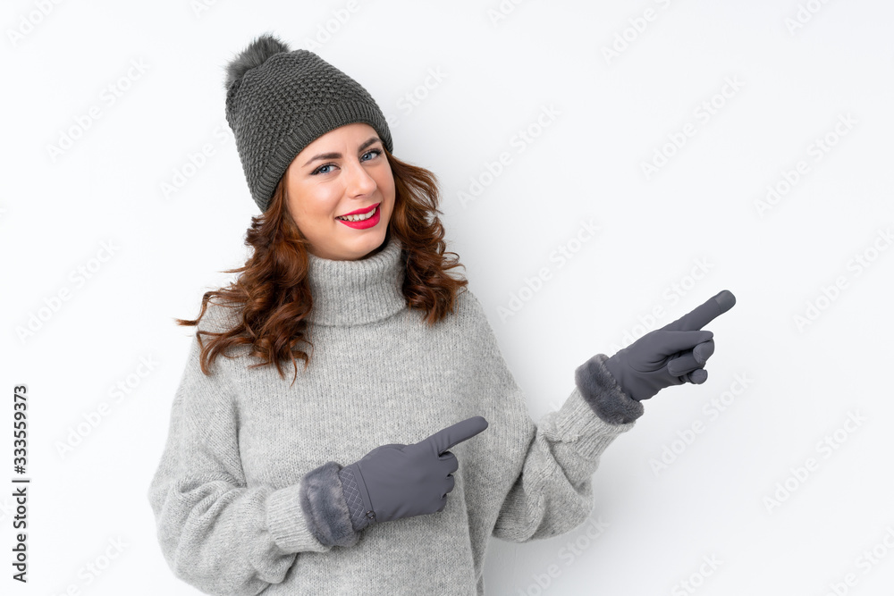 Wall mural young russian woman with winter hat over isolated white background pointing finger to the side