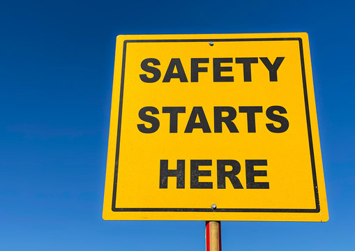 Yellow sign with text Safety Starts Here against blue sky - Powered by Adobe