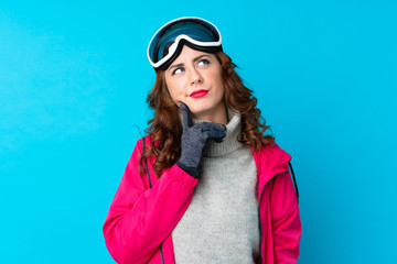 Skier woman with snowboarding glasses over isolated blue wall thinking an idea