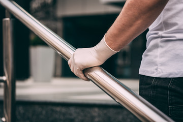 Male hand in a white latex medical glove on the railing..man wearing protective latex gloves touching railing outsid