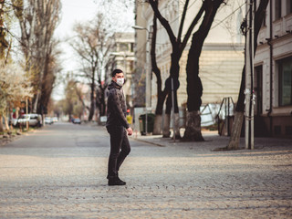 Fototapeta premium Cowid-19 virus. A man in a medical mask is walking on an empty street in the city. Pandemic mask virus protection.