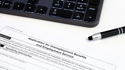 Application for employment benefits form with computer keyboard and pen on white background. Unemployment rate has risen sharply in United States due to closed business caused by corona virus outbreak