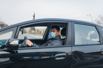 Fototapeta na wymiar a man driving a car puts on a medical mask during an epidemic, a taxi driver in a mask, protection from the virus. Driver in black car. coronavirus, disease, infection, quarantine, covid-19