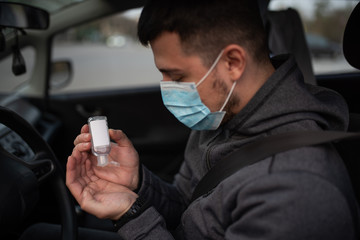 A man use an antiseptic gel into his hands while sitting in a car. A man in a medical mask to protect viruses. masked man in a car. coronavirus, disease, infection, quarantine, covid-19